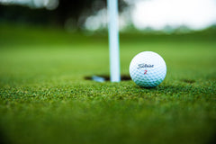 Close-up of a golf ball resting near the hole on a putting green, with the flagstick in view