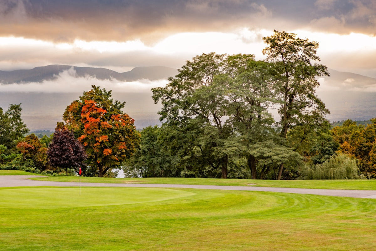 A golf course during autumn, with vibrant fall foliage, rolling fairways, and misty mountains in the background.
