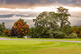 A golf course during autumn, with vibrant fall foliage, rolling fairways, and misty mountains in the background.