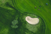 An aerial view of a golf course with a sand bunker and green fairways, highlighting a professional golfing experience.