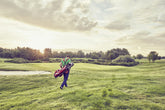A golfer walking towards the tee box on a professional golf course, preparing for the first shot of the day.