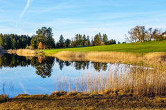 A scenic golf course featuring a calm pond surrounded by lush greenery and a peaceful atmosphere.