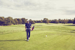 A golfer walking along the green fairway, carrying a bag of clubs, experiencing a peaceful golf session.