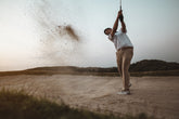 A golfer taking a bunker shot at sunset, enjoying a high-end golf experience.