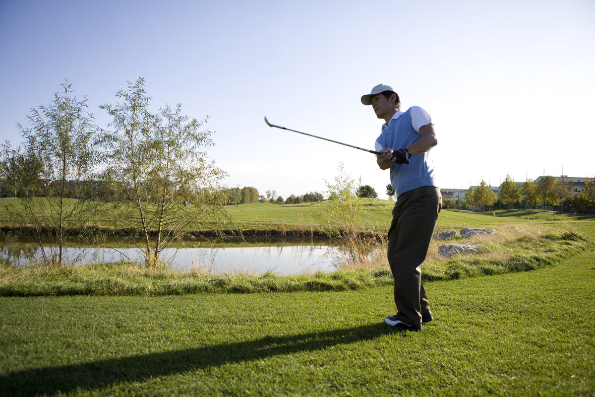A golfer in mid-swing, focusing on hitting a perfect shot under a clear blue sky on a premium golf course.