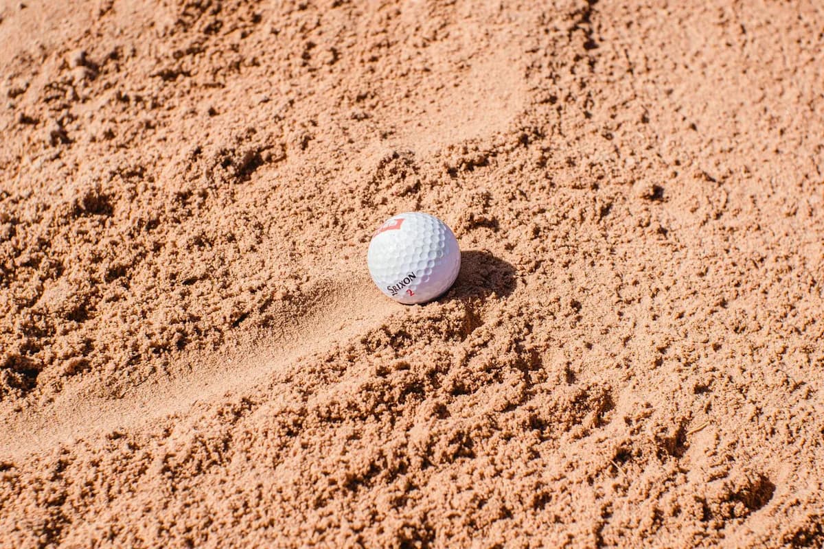 A golfer playing a sand shot from a greenside bunker with a spray of sand