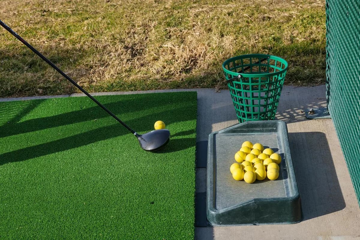 A golfer hitting balls at a driving range with a bucket of balls beside them