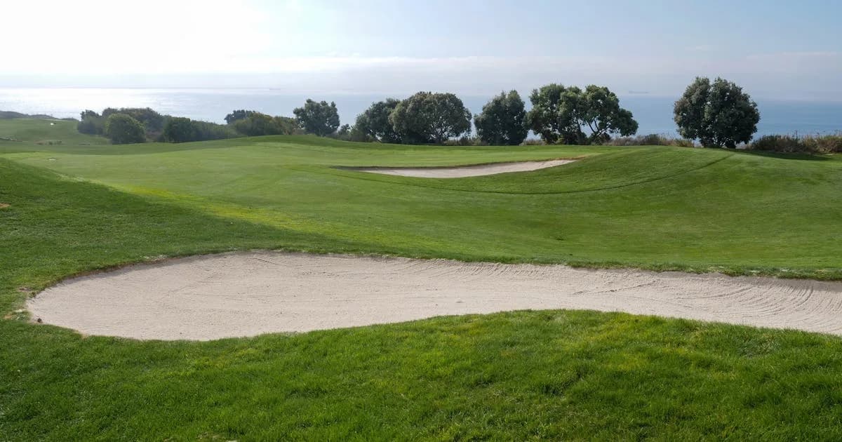 Golf course with sand trap and ocean view under a clear blue sky