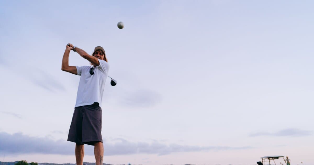 A golfer in a balanced follow-through against an evening sky, ball in flight