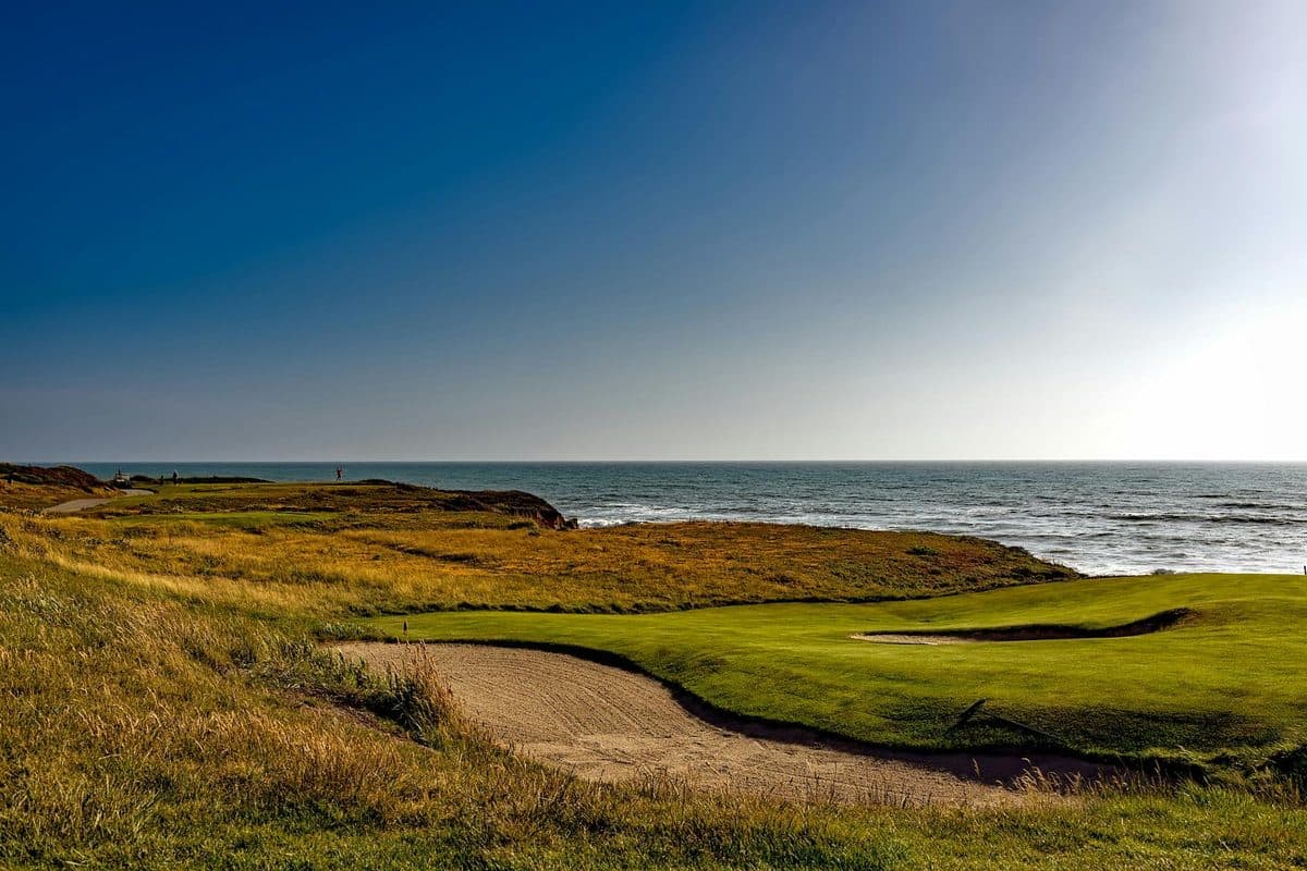 A golfer playing a shot on an exposed links course with a clear sky and strong wind