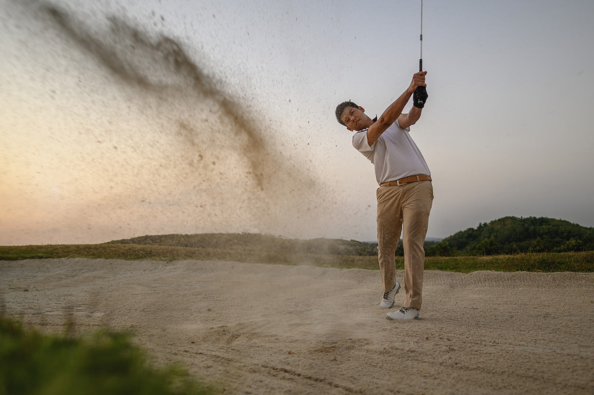 A golfer hitting from a bunker, sending sand flying as they execute a perfect escape shot.