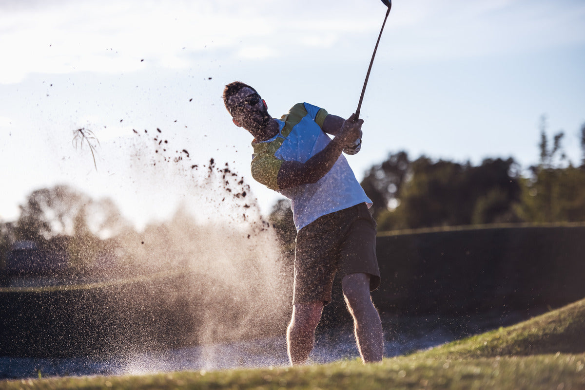 A golfer hitting a bunker shot, sending sand into the air, during a golf experience.