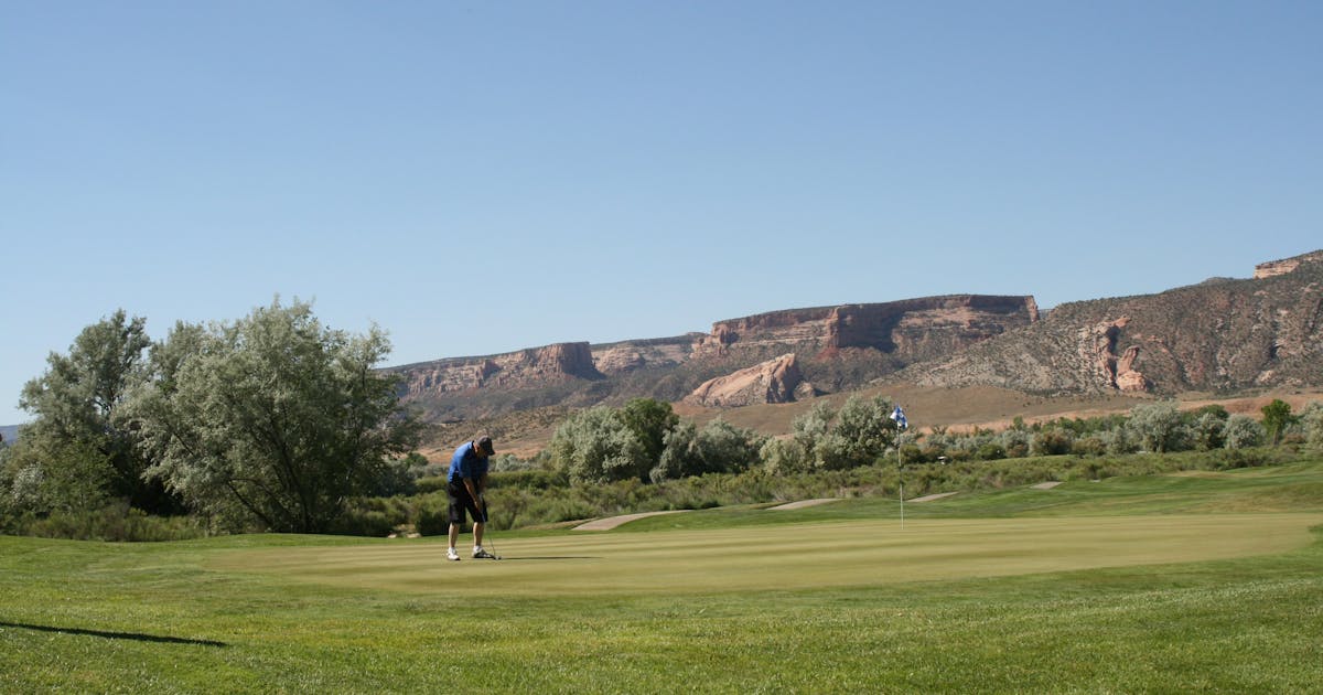A dramatic view down a golf fairway lined with trees on a clear afternoon