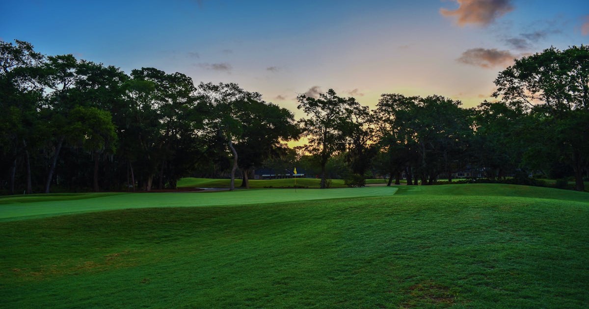 A golfer walking down a dramatic tree-lined fairway at a prestigious course