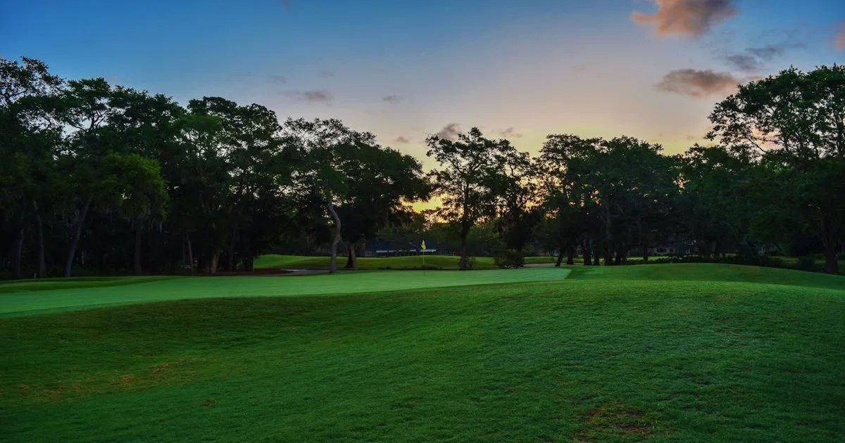 A golfer walking down a dramatic tree-lined fairway at a prestigious course