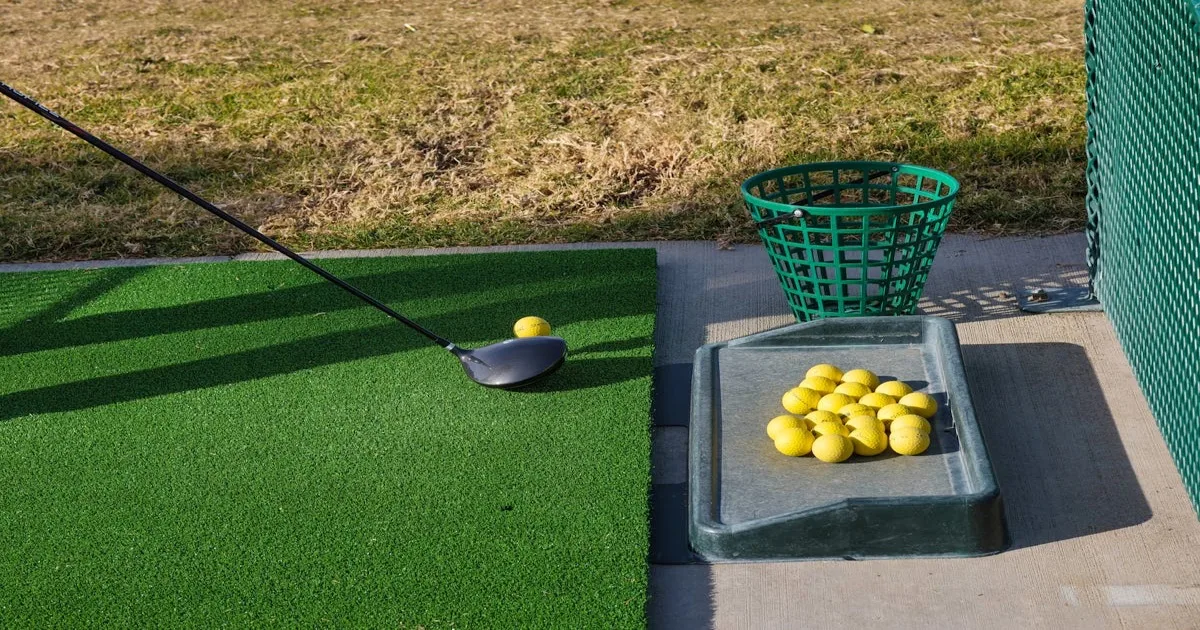 A golfer practising their swing on a driving range with an instructor nearby