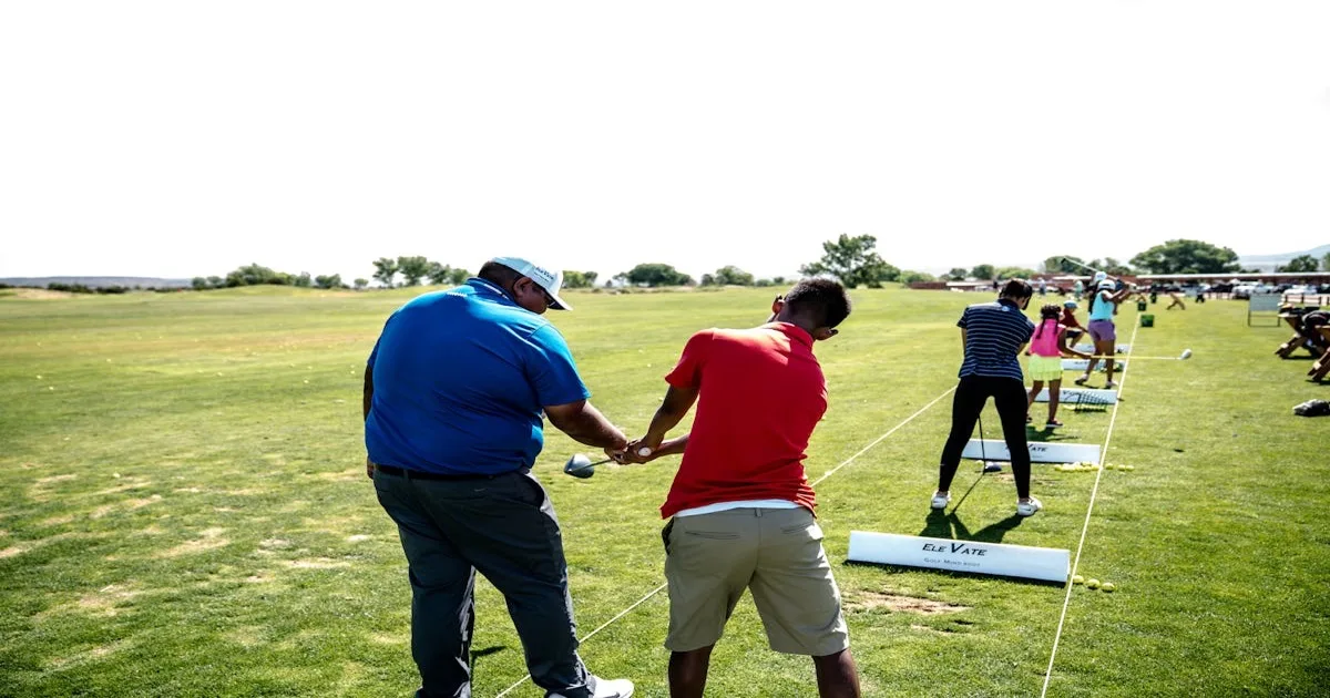 A golf instructor demonstrating a swing to a beginner on a practice range