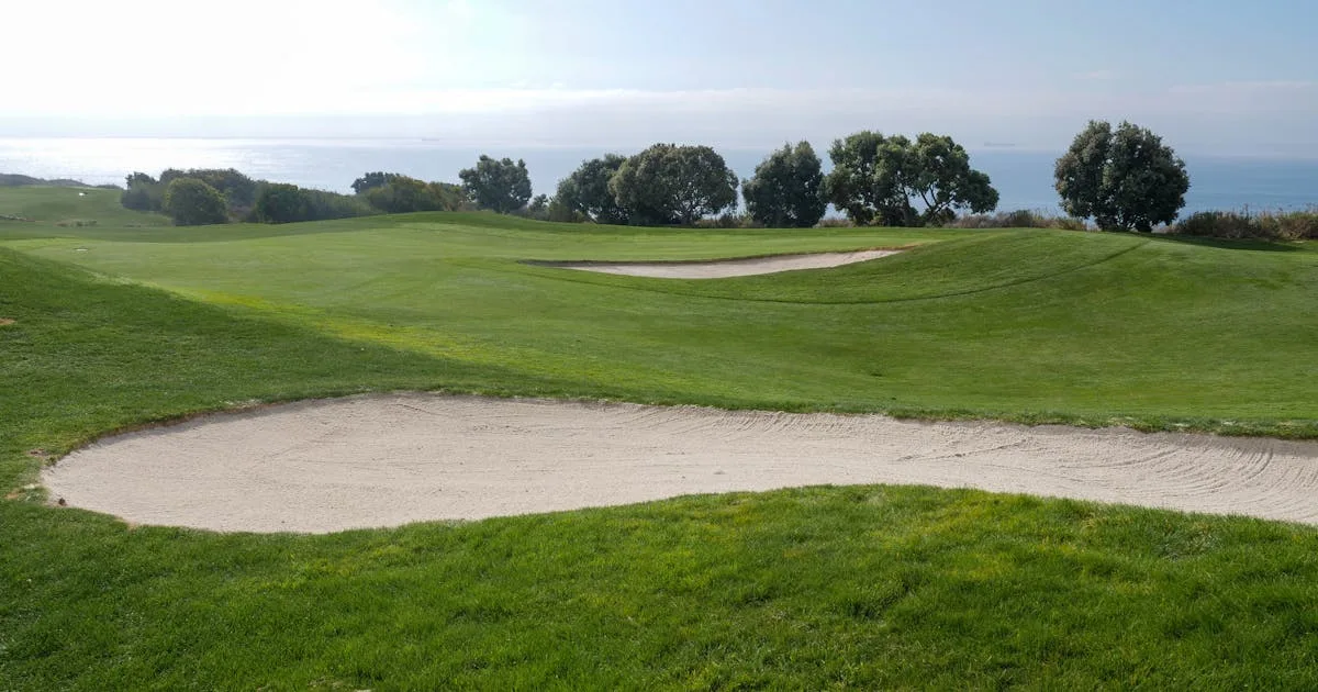 A dramatic links golf course with sand traps and ocean view under blue skies