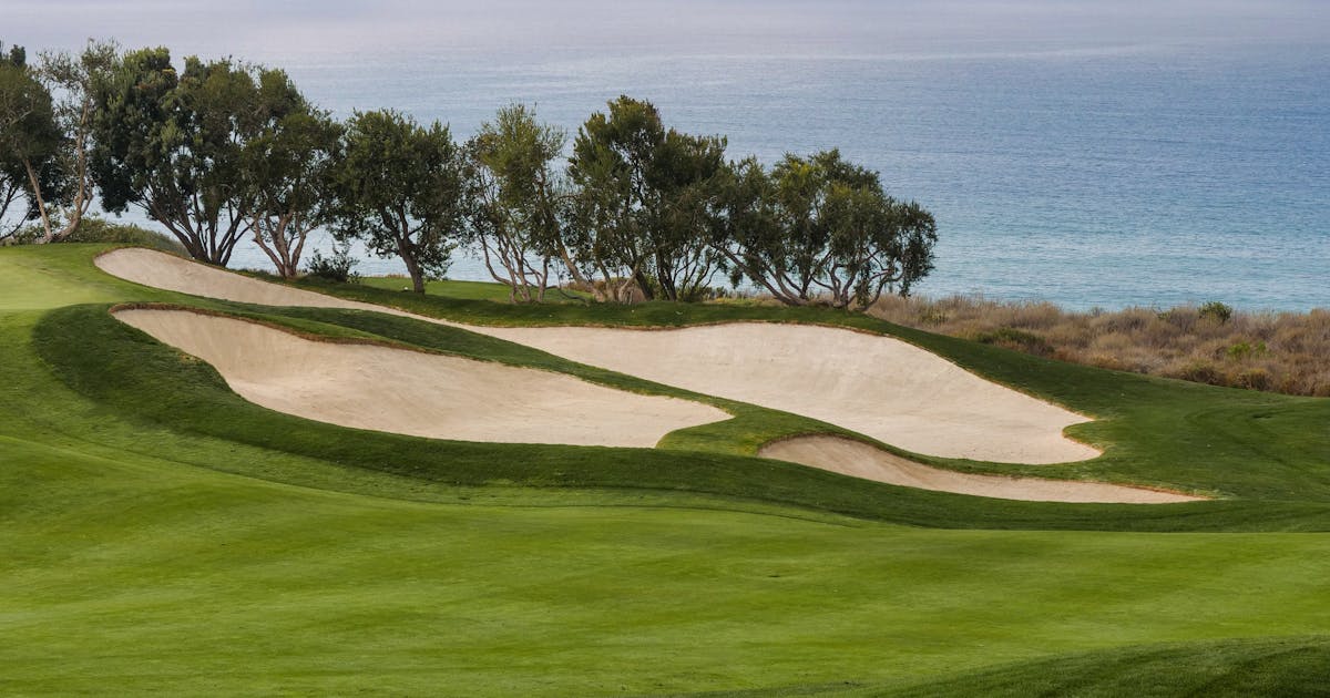 A coastal golf course with green fairway and sandy bunkers under a cloudy sky