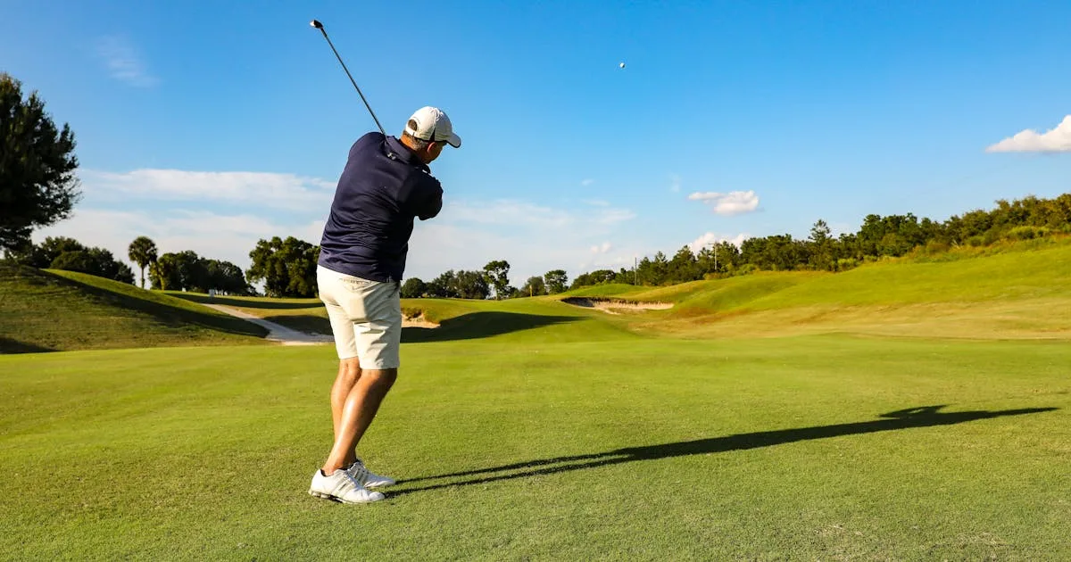 A golfer swinging a driver on a well-maintained golf course on a bright day