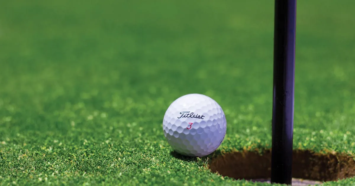 Close-up of a golf ball on the lip of the cup on a well-maintained green